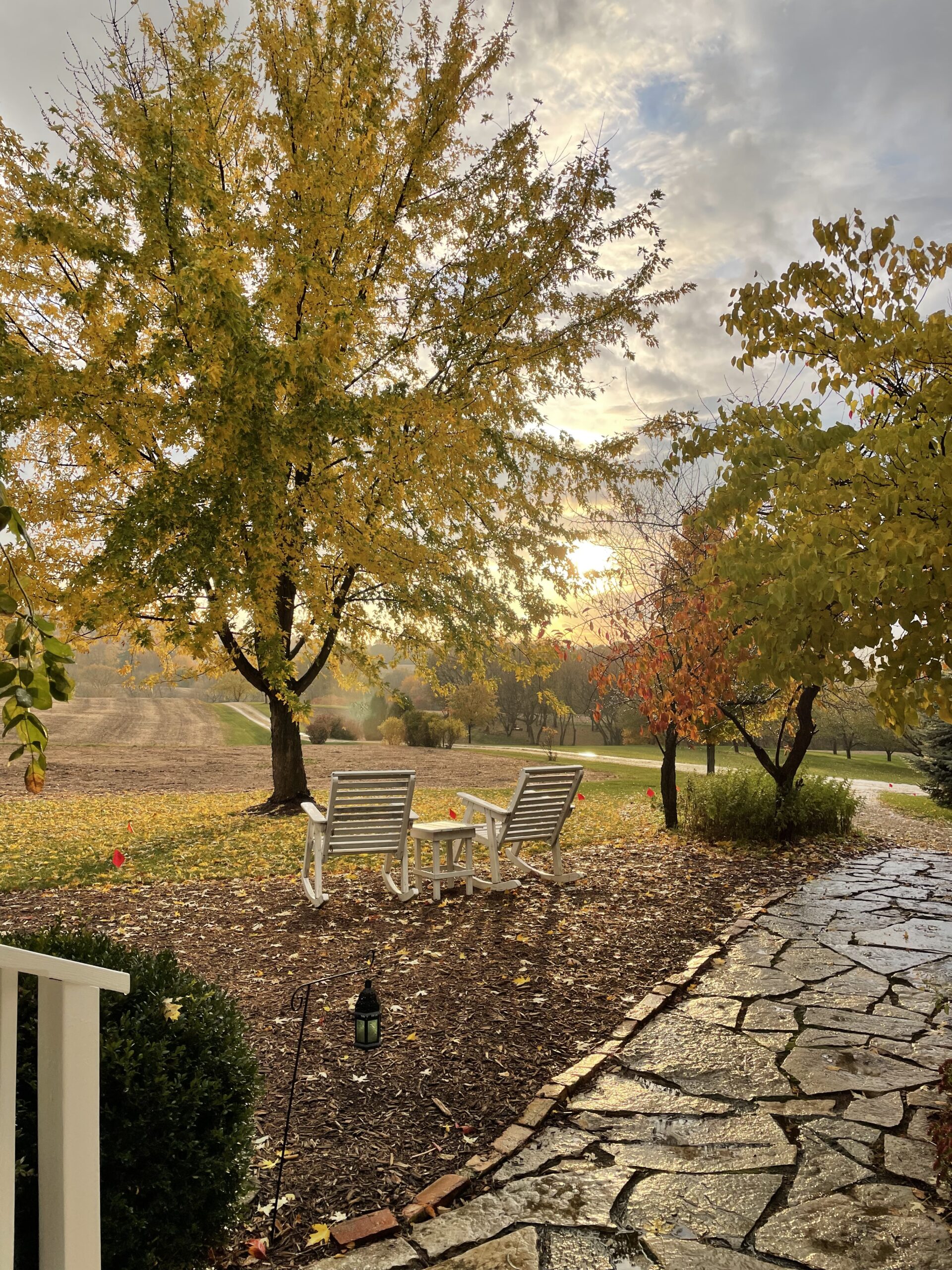 Autumn sunset in distance, stone path and white rocking chairs in foreground